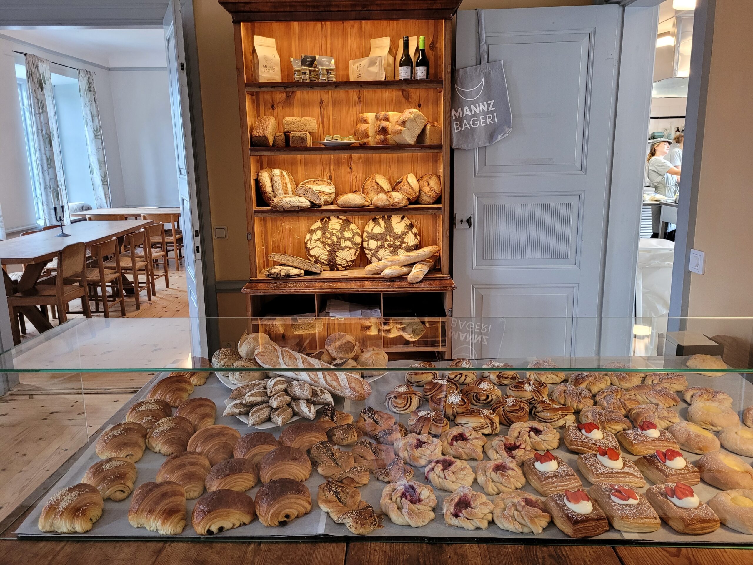 Interior from the cafe with pastries in the background. Behind a shelf with bread and to the left you can see part of the dining room.