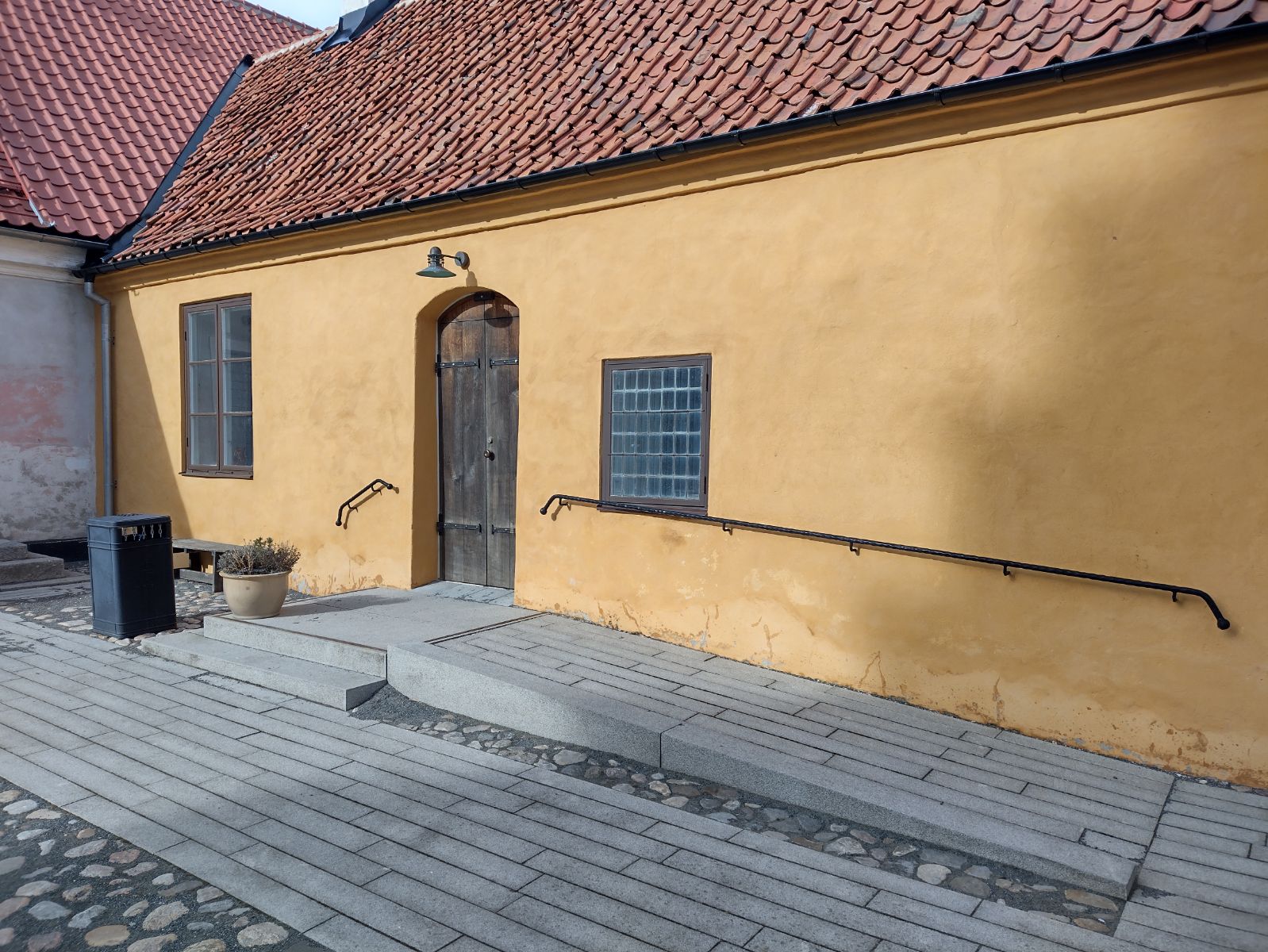 A house with yellow-orange lime plaster and red roof tiles is seen obliquely from the front from the castle yard. A ramp runs along the right side of the building up to the door in the middle.