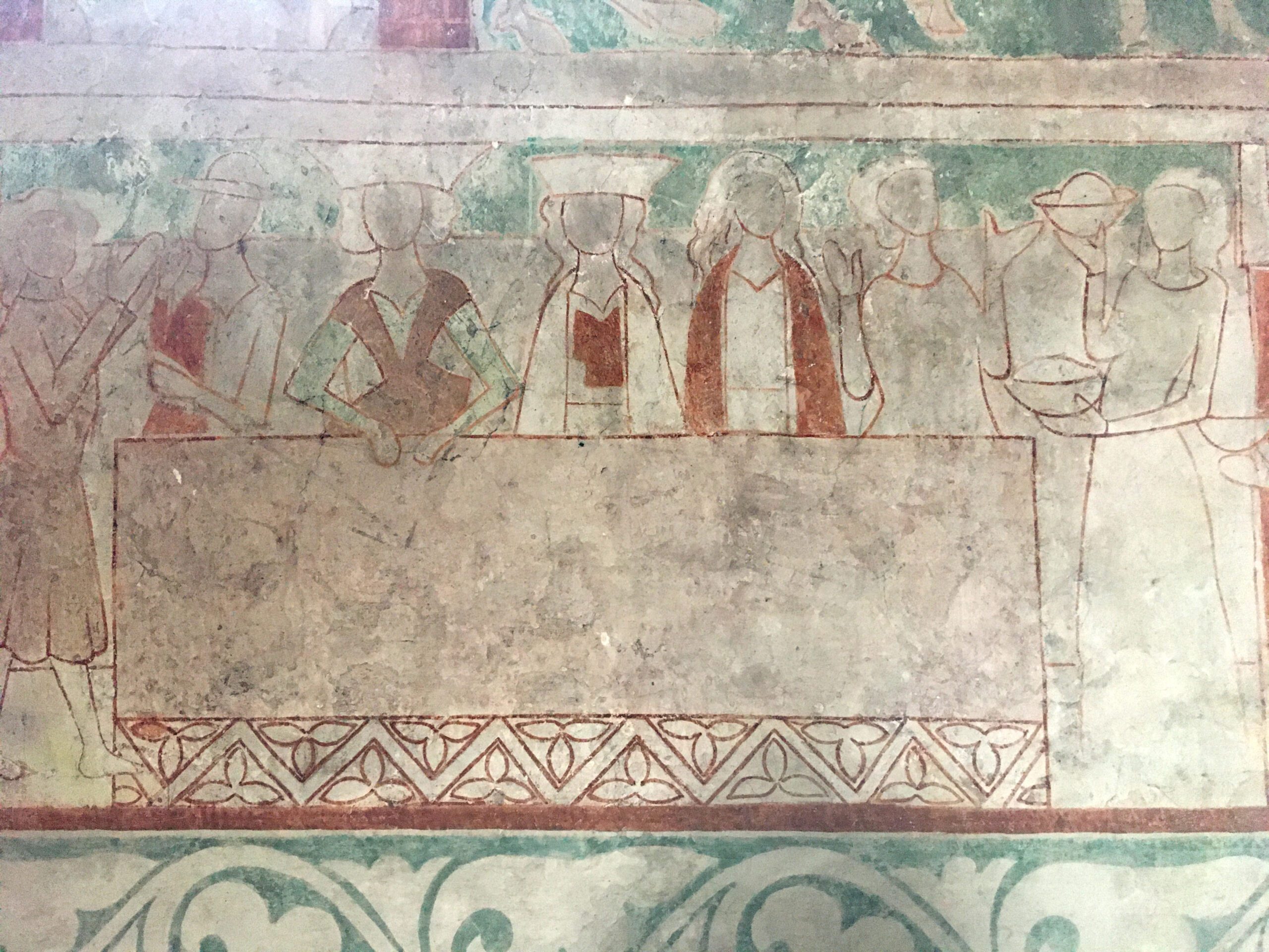 A medieval chalk painting in red, white and green shows a group sitting at a table, where they are being served.