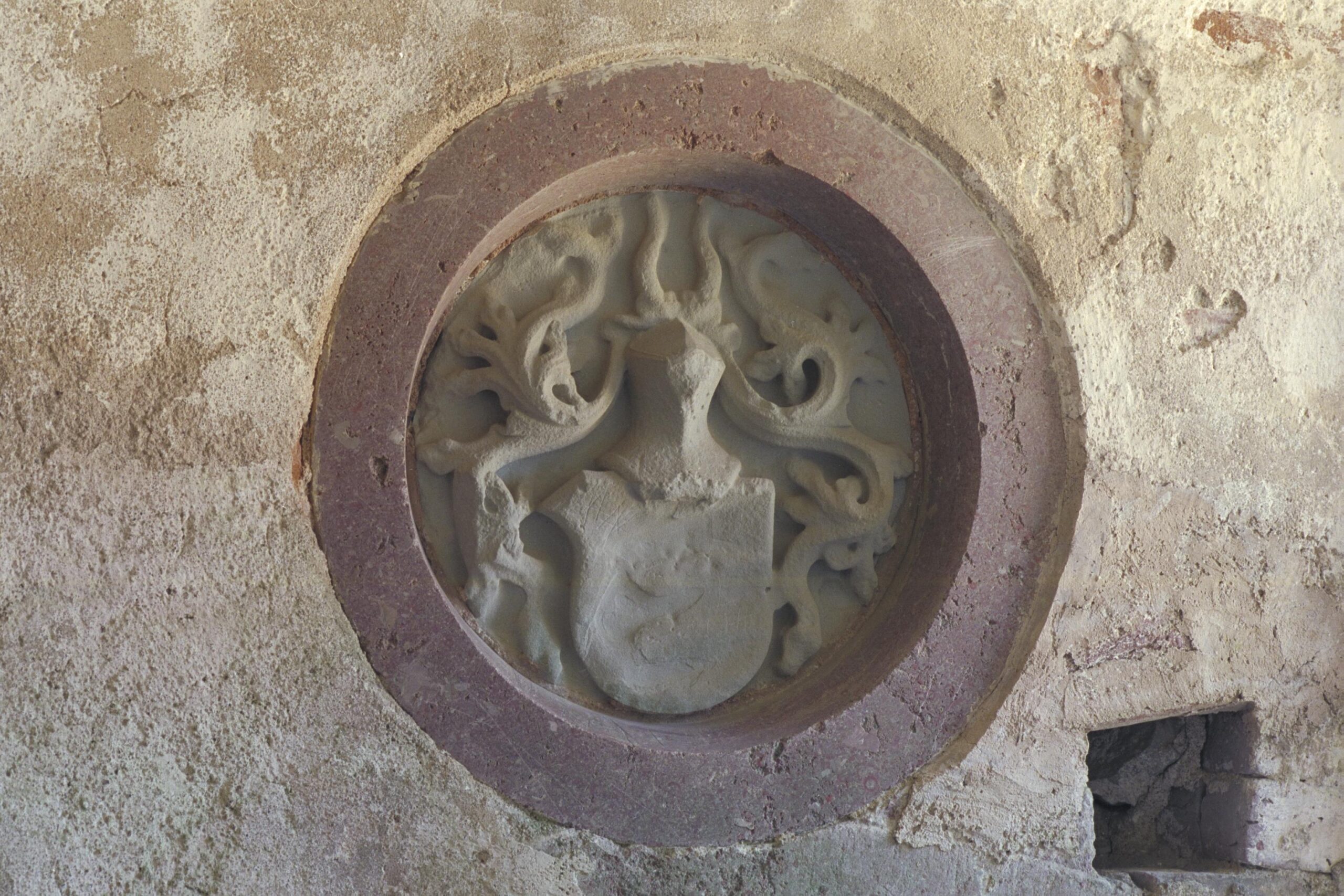 Vapensköld krönt av en rustningshjälm, hugget i sten, på en vägg.