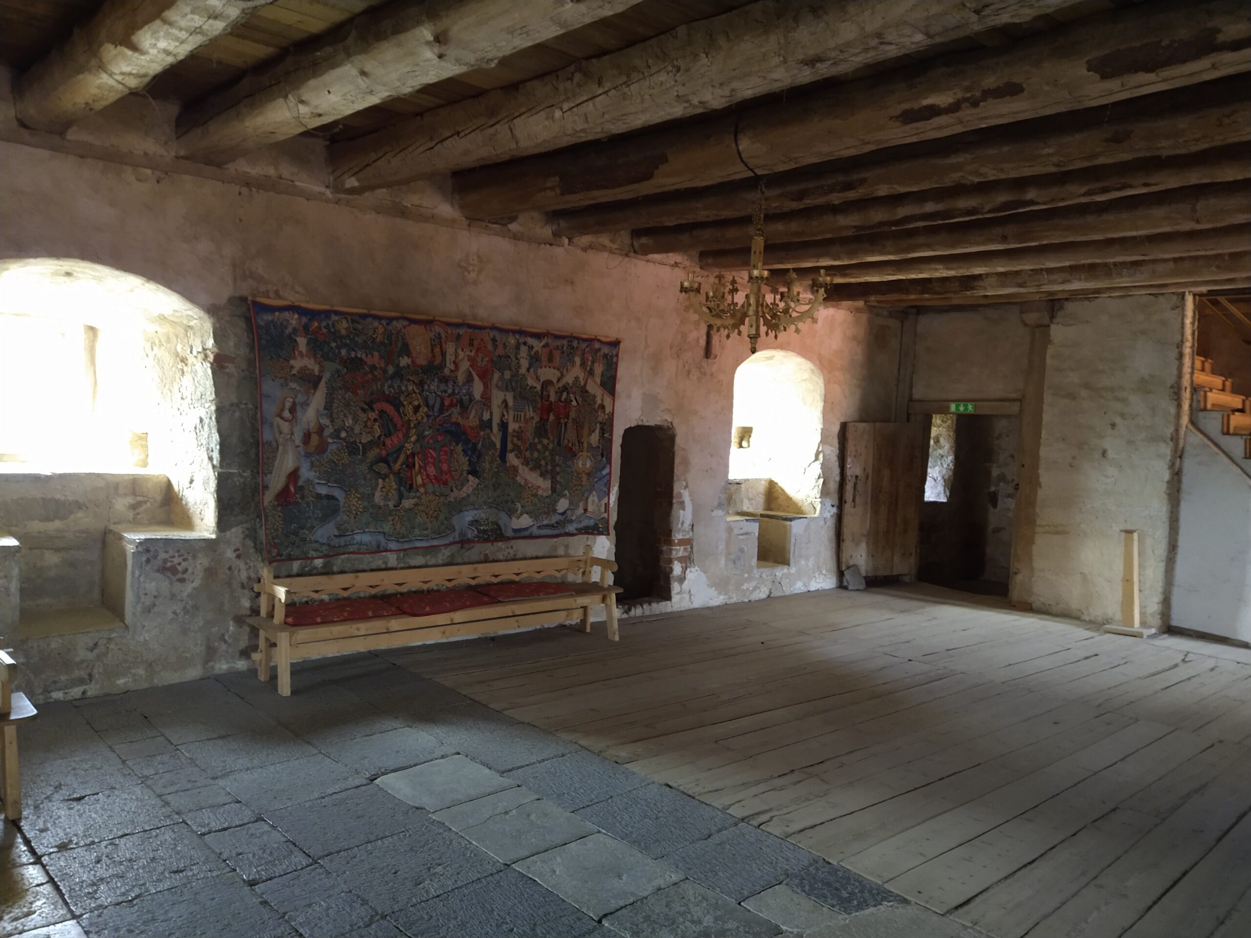 Here you can see part of the great hall with a tapestry on the wall and a bench underneath. Wooden beams can be seen in the ceiling.