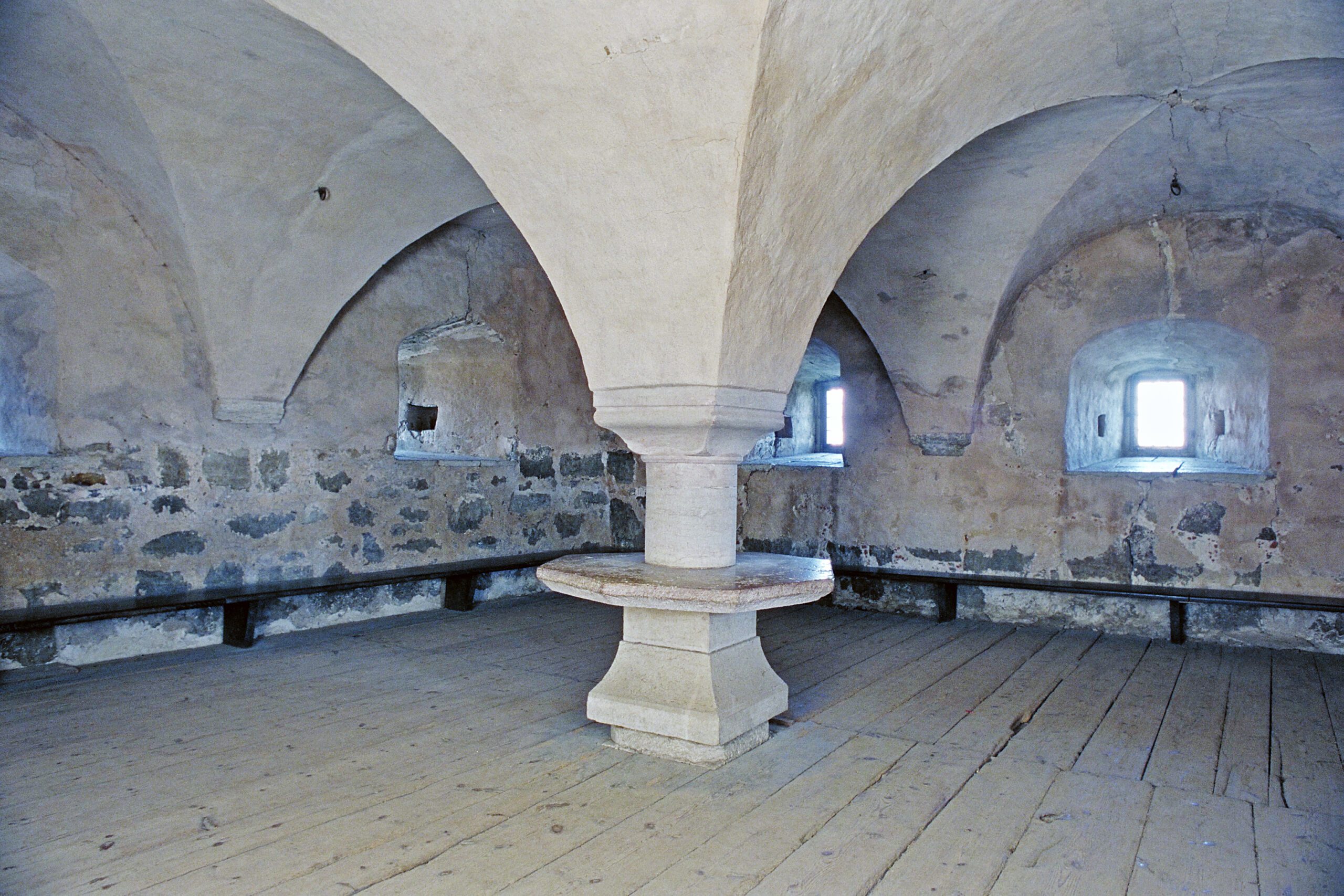 Here, the castle hall is shown, whose vault descends into a pillar with a table top in the middle. Benches run along the walls and the floor is made of wood.