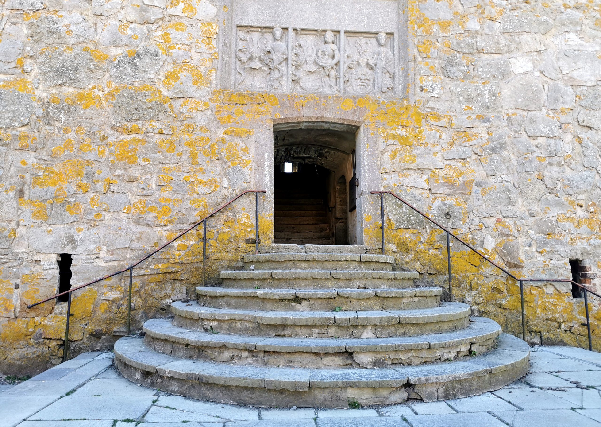 The picture shows the castle gate with the stairs at the bottom of the picture, as well as the gate in the middle with a stone tablet above.