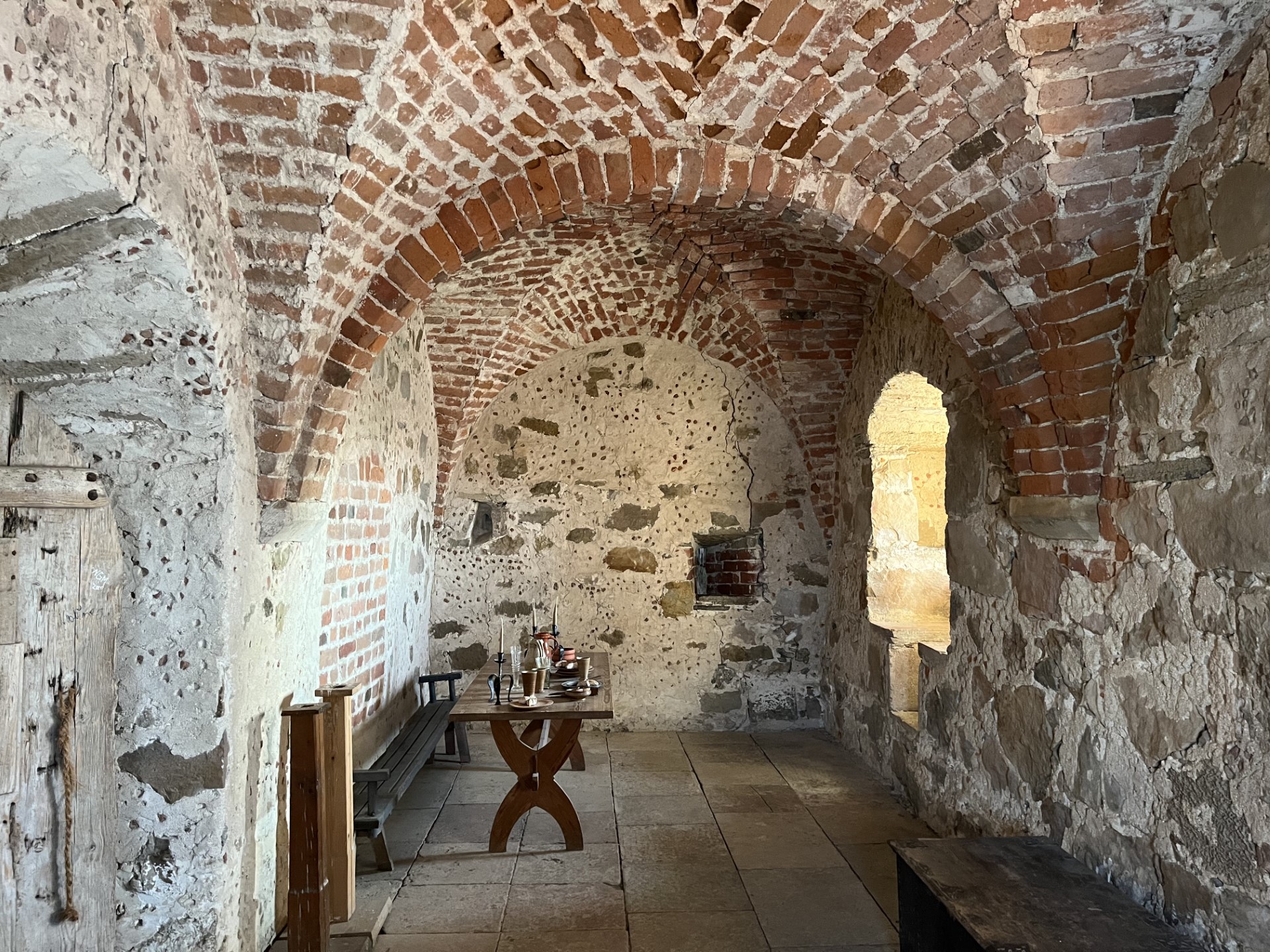 The picture shows a long, narrow room in the castle with a brick vault. Along the long sides are furniture such as a chest, bench and chair.